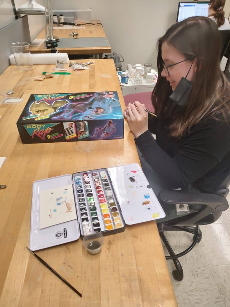Elizabeth Kidder inpainting on a Body Wrap box during her internship. 