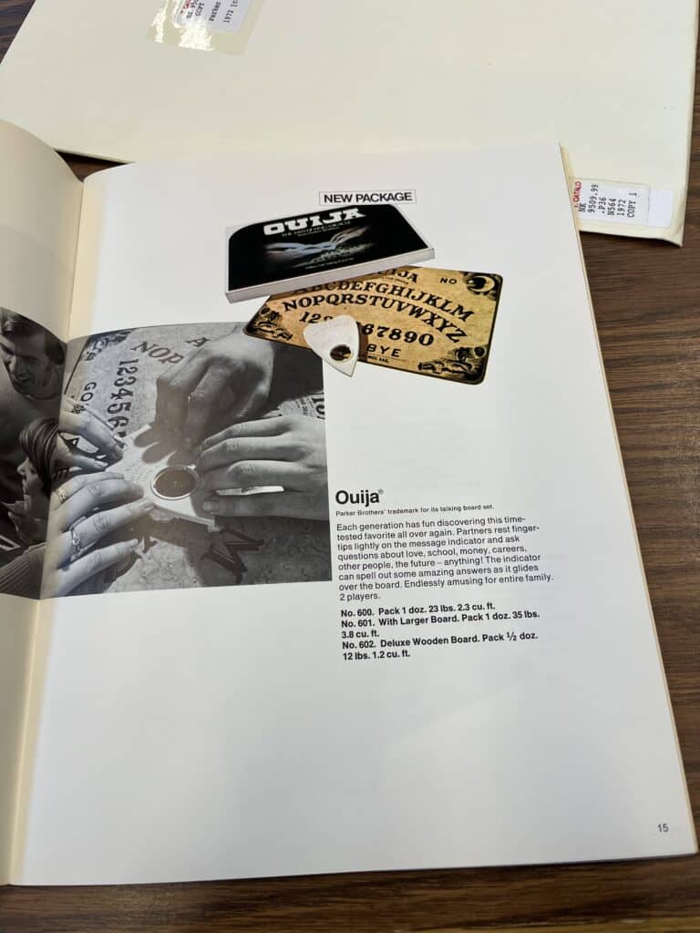 Illustration of An advertisement for Ouija in the 1972 issue of Parker Brothers catalog. The “blue ghost” box has been replaced with an image of several hands holding a planchette, and the accompanying divination games are no longer being advertised. 